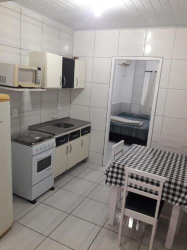 a white kitchen with a stove and a table and a microwave at Apartamentos C. Santos in Penha