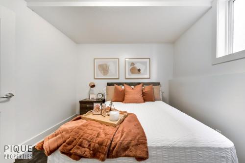 a white bedroom with a bed with a orange blanket at Stunning Modern Suite - King Bed - Free Parking & Netflix - Fast Wi-Fi - Long Stays Welcome in Edmonton