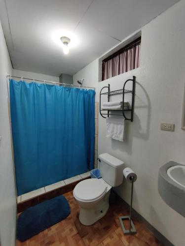 a bathroom with a toilet and a blue shower curtain at Cabinas Maritza in Quebrada Ganado