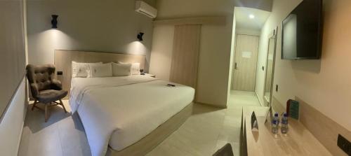 a bedroom with a large white bed and a chair at Hangar Inn Guadalajara Aeropuerto in Guadalajara