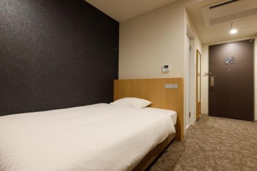a bedroom with a large white bed and a door at Plum Hotel in Osaka