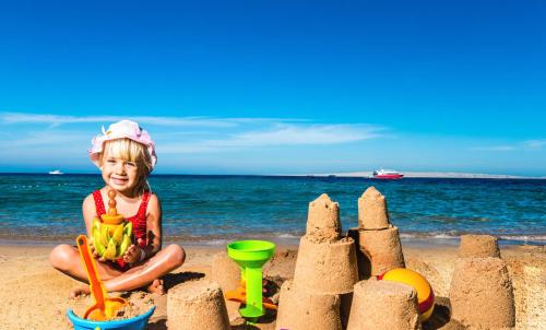a little girl sitting on the beach with a sand castle at Seagull Beach Resort - Families and Couples Only in Hurghada