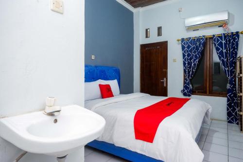 a bathroom with a white sink and a bed with a red blanket at RedDoorz at Pakuncen Malioboro Yogyakarta in Yogyakarta