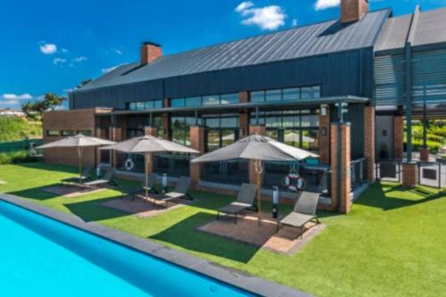 a building with chairs and umbrellas next to a pool at The Parks Airport Apartment in Boksburg