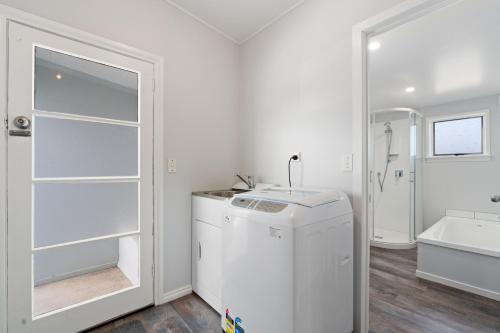 a white bathroom with a refrigerator and a sink at Lake Dunstan Cottage - Cromwell Holiday Home in Cromwell
