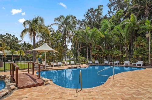 a pool at a resort with chairs and an umbrella at Lorikeet Holiday Park in Arrawarra