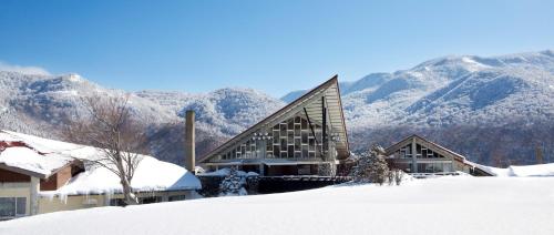 a building in the snow with mountains in the background at Okushiga Kogen Hotel in Yamanouchi