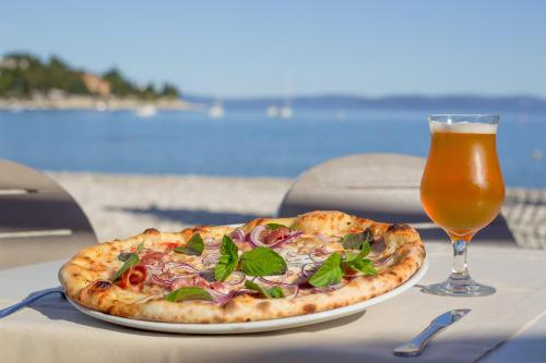 eine Pizza auf einem Tisch neben einem Glas Bier in der Unterkunft Hotel Narcis - Maslinica Hotels & Resorts in Rabac