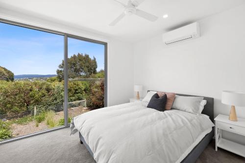 a white bedroom with a bed and a large window at Aireys Sunset Beach House in Aireys Inlet