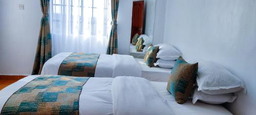 2 camas en una habitación con sábanas y almohadas blancas en The Crooner Lounge, en Nairobi