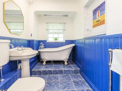 Haven Cottage في Berrow: حمام باللون الأزرق والأبيض مع حوض استحمام ومغسلة