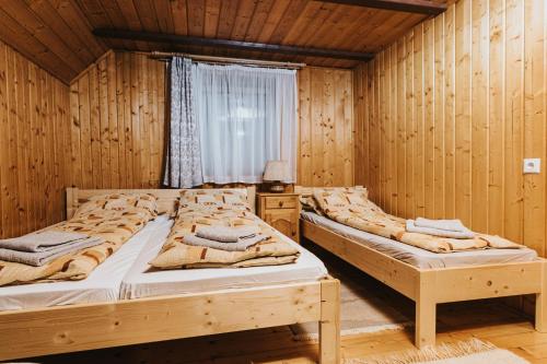 2 Betten in einem Holzzimmer mit Fenster in der Unterkunft Súgópatak Kulcsosház in Izvoare