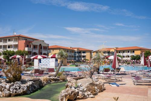 um resort com uma piscina com cadeiras e guarda-sóis em Pini Village Lido Altanea em Caorle