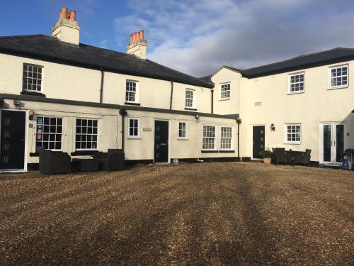 a large white house with black doors and a dirt yard at Whitehouse Holiday Lettings - Luxury Serviced Properties in St Neots, Little Paxton and Great Paxton in Saint Neots