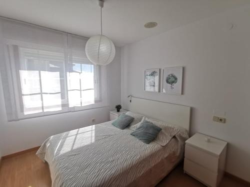 a white bedroom with a bed and a window at Playa Panadeira, piso céntrico in Sanxenxo