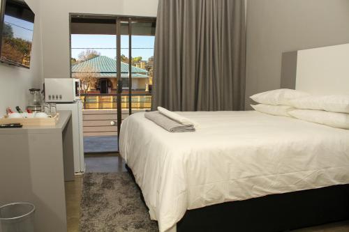 1 dormitorio con cama blanca y ventana en Alu Boutique Hotel and Conference en Roodepoort