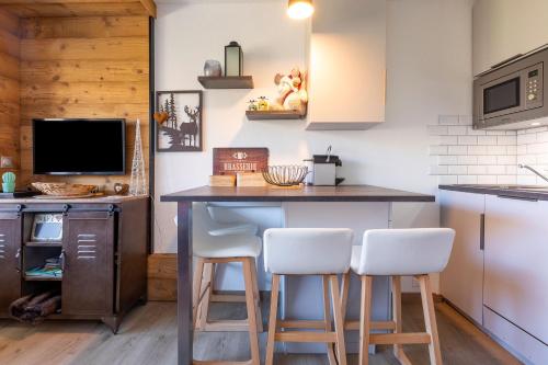 a kitchen with a bar with white stools at Résidence Le Necou - Les Ménuires in Les Menuires