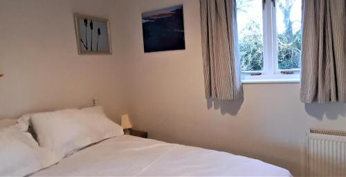 a bedroom with a white bed and a window at Garden Cottage, Five Pines in Acton Turville