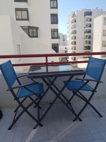 a glass table and two blue chairs on a balcony at Apartamento Batalha - Quarteira, Algarve, Portugal in Quarteira