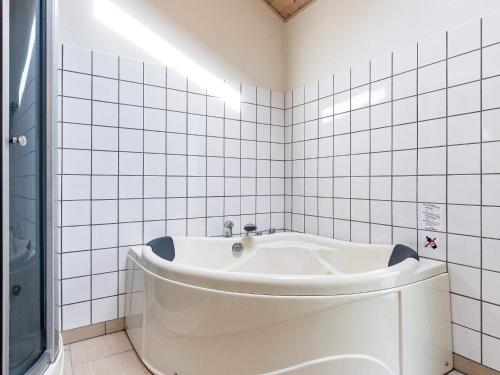 a white bath tub in a white tiled bathroom at Four-Bedroom Holiday home in Ålbæk 4 in Ålbæk