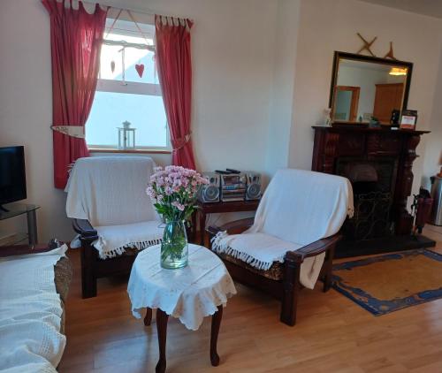 a living room with two chairs and a vase of flowers on a table at Rockgardencottage in Lettermacaward