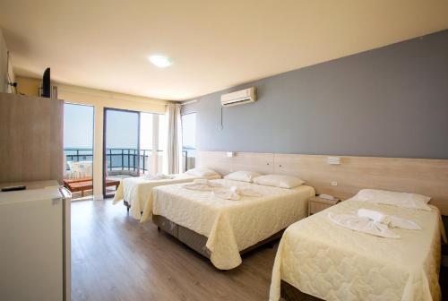 a hotel room with three beds and a balcony at Hotel Vila Mar in Florianópolis
