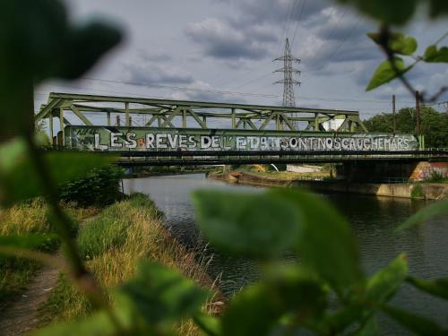 a bridge with a sign on it over a river at Adventure Alternative - GUEST HOUSE - Arts-Factory-Experience - For artists, makers and open minds - Attention, we are not a hotel and are not adapted for everybody - Read host warnings before reservation - PROVIDENCE,BE asbl in Charleroi