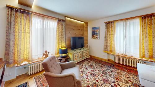 a living room with a chair and a tv and windows at Chesa Centrum in Celerina