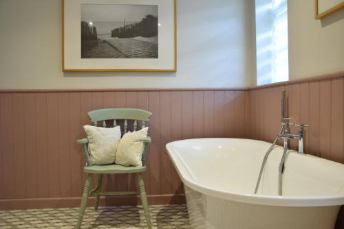 a bath tub and a chair in a bathroom at Satis Cottage, Westleton in Westleton