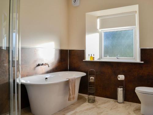 baño con bañera, aseo y ventana en Liftingstane Dairy Cottage, en Closeburn