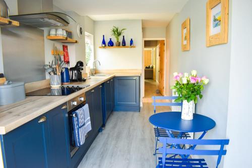 une cuisine avec des placards bleus et une table fleurie. dans l'établissement Seagull Cottage - Suffolk Coastal Escapes, à Pakefield