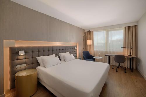 ein Hotelzimmer mit einem großen weißen Bett und einem Schreibtisch in der Unterkunft NH Lyon Airport in Saint-Exupéry