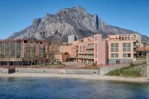 a building with a mountain in the background with water at NH Lecco Pontevecchio in Lecco