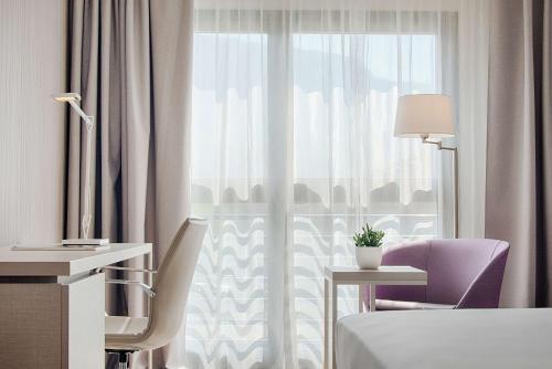 um quarto de hotel com uma cama e uma cadeira e uma janela em NH Lecco Pontevecchio em Lecco