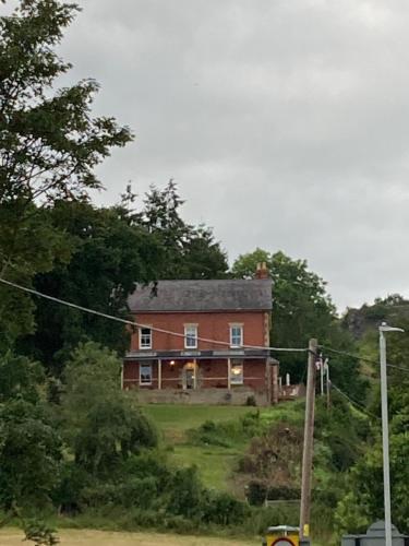 a large brick house on a hill with trees at Penyvoel Hall in Llanymynech