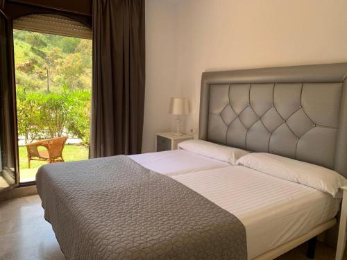 une chambre avec un grand lit avec une grande fenêtre dans l'établissement Apartamento espacioso muy tranquilo con piscinas y jardines cercano a la playa, à Estepona