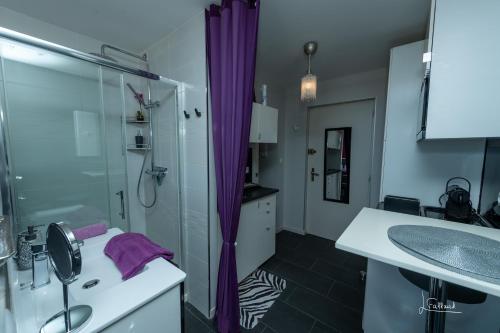 La salle de bains est pourvue d'un lavabo et d'une douche avec des rideaux violets. dans l'établissement Studio Glamour Naturiste, au Cap d'Agde