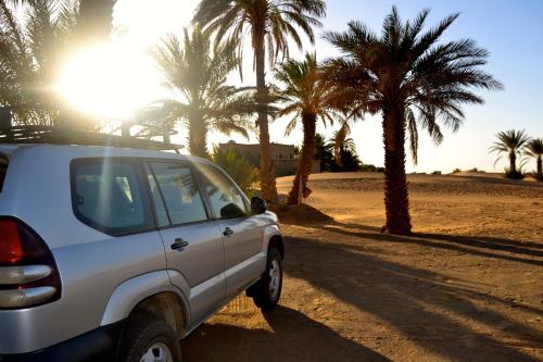 a car parked on the side of a road with palm trees at Kanz Erremal in Merzouga