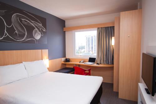 a hotel room with a bed and a desk with a laptop at ibis Mogi das Cruzes Shopping in Mogi das Cruzes