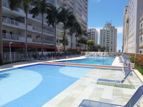 una grande piscina con sedie e palme di GUARUJÁ ASTURIAS, LAZER COMPLETO, AR CONDICIONADO E VARANDA GOURMET a Guarujá