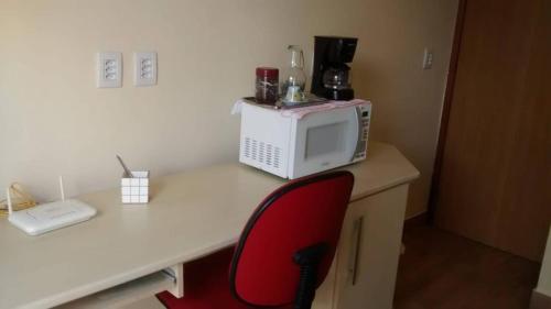 a red chair sitting at a desk with a microwave at Suíte residencial com entrada independente em Itatiba in Itatiba
