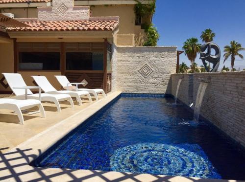 a swimming pool with white chairs next to a house at Cabo Vista Hotel Adults Only in Cabo San Lucas
