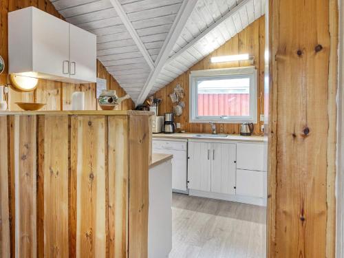 a kitchen with wooden walls and white cabinets and a window at Holiday Home Dyssestræde in Dannemare