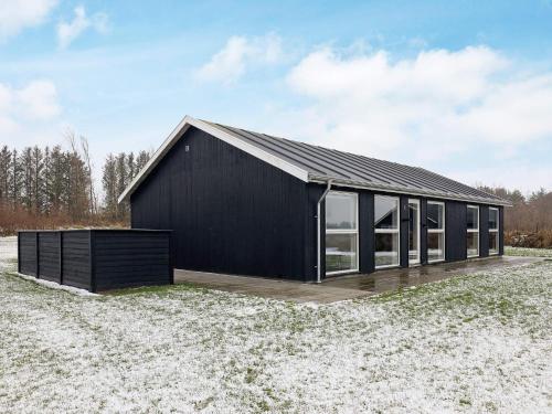 uma casa preta com um deque de madeira num campo em 6 person holiday home in L kken em Lokken