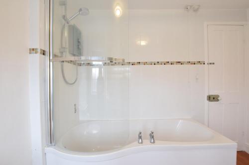 a white bath tub in a bathroom with a shower at 1 Tailors Cottage, Woodbridge in Woodbridge