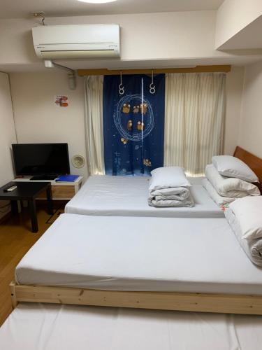 two beds in a room with a desk and a television at Sophiearth Apartment in Tokyo