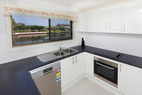 a kitchen with white cabinets and a sink and a window at Lake House on Elouera in Forster