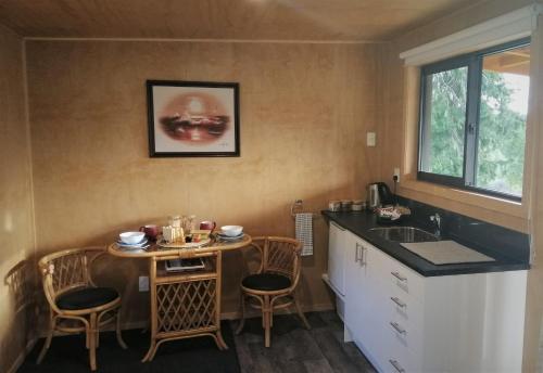 een keuken met een wastafel en een tafel met stoelen bij Glenwood Akaroa Bush Retreat - Totara Hut in Akaroa