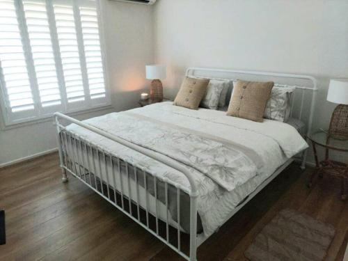 a white bed in a bedroom with two windows at White Cottage on Ninety Mile Beach in Seaspray