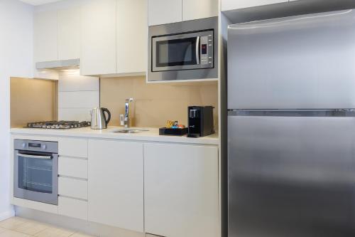 cocina con nevera de acero inoxidable y microondas en Meriton Suites Zetland en Sídney